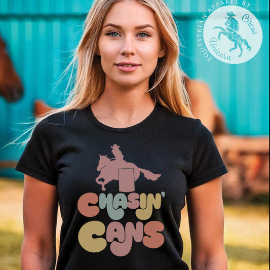 Woman wearing a black barrel racing t-shirt with colorful text and graphic, standing in front of a turquoise barn with a quarter horse.